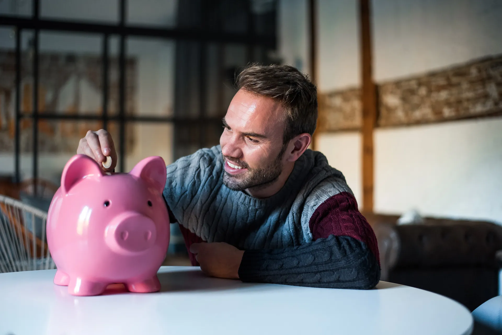 Mann steckt eine Münze in ein rosa Sparschwein